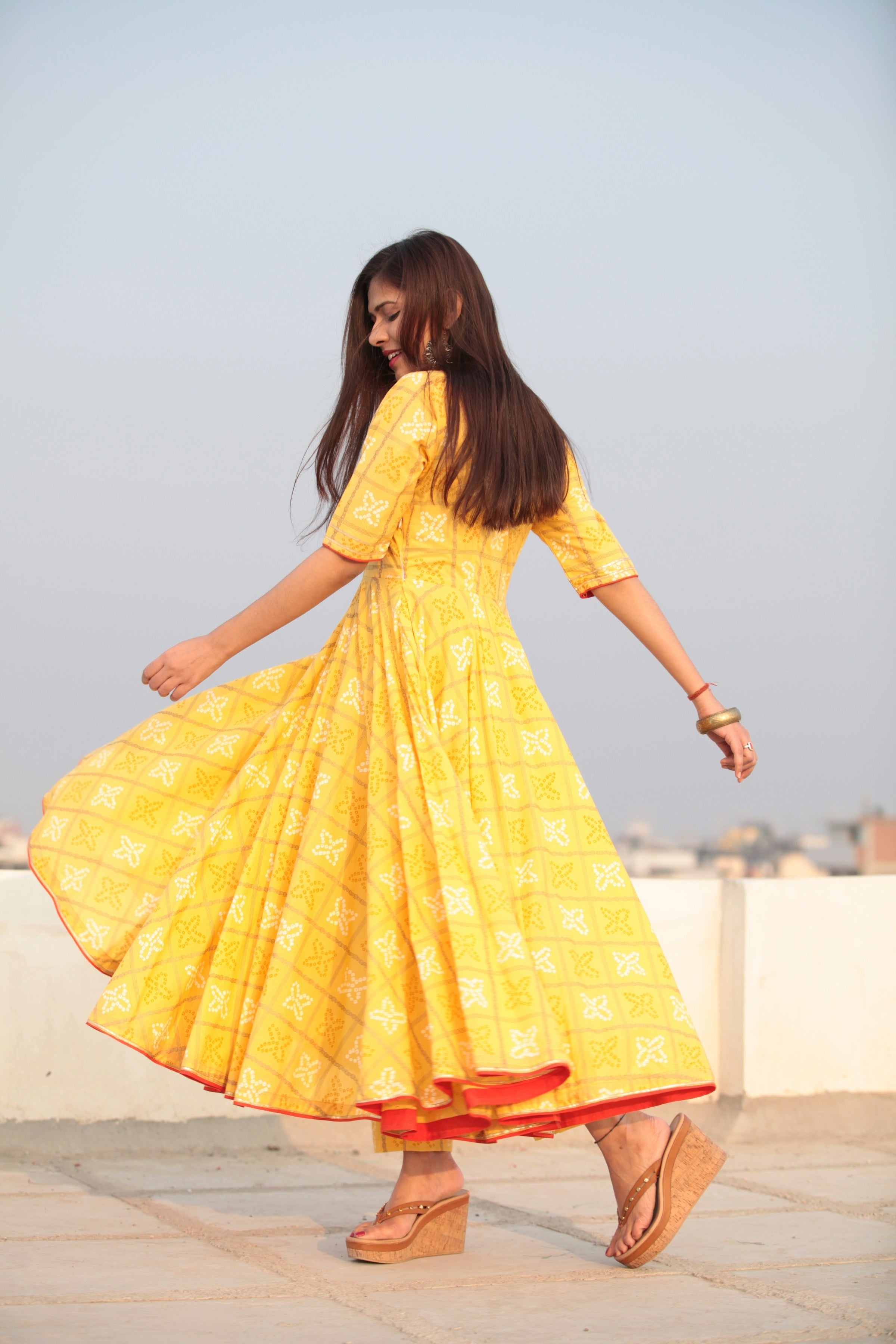 Woman twirling in a vibrant saffron yellow flared designer maxi dress